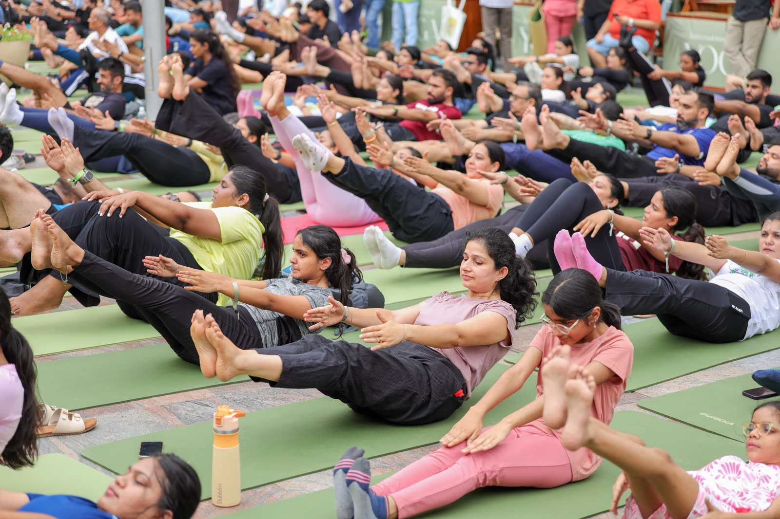 A large crowd holding a seated boat pose together at International Day of Yoga